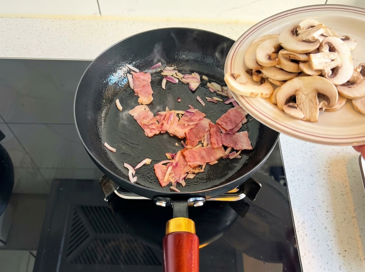 In Scheiben geschnittene Champignons werden von einem Teller in die Pfanne zu den Zwiebeln und dem Speck geschoben.