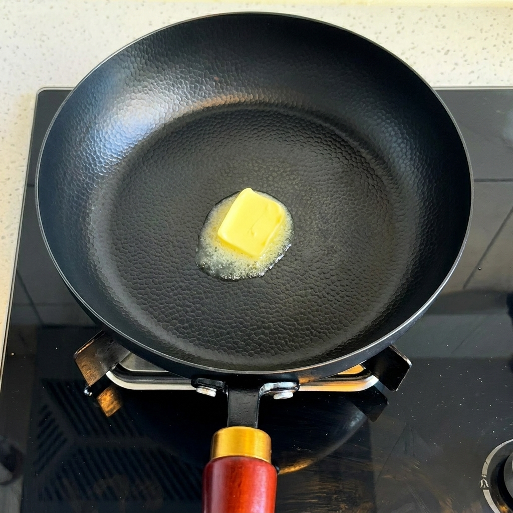 Ein quadratisches Stück gelbe Butter schmilzt in einer heißen schwarzen Pfanne.