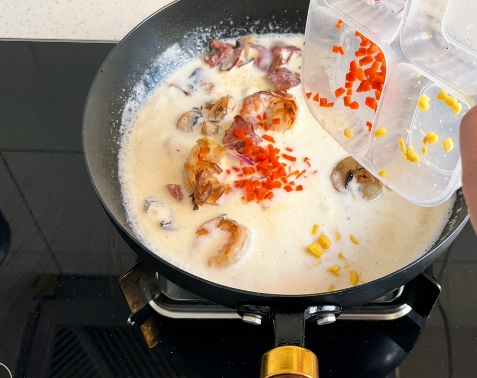 Karottenwürfel und Maiskörner werden aus einem Behälter in die sprudelnde Cremesuppe gegeben.