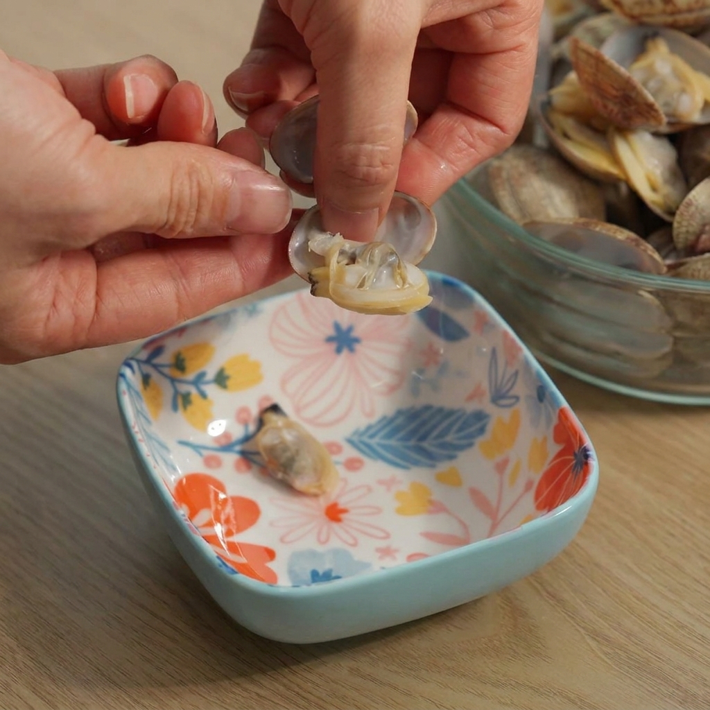 Hände lösen vorsichtig das Fleisch einer gekochten Muschel aus der Schale über einer Schüssel.