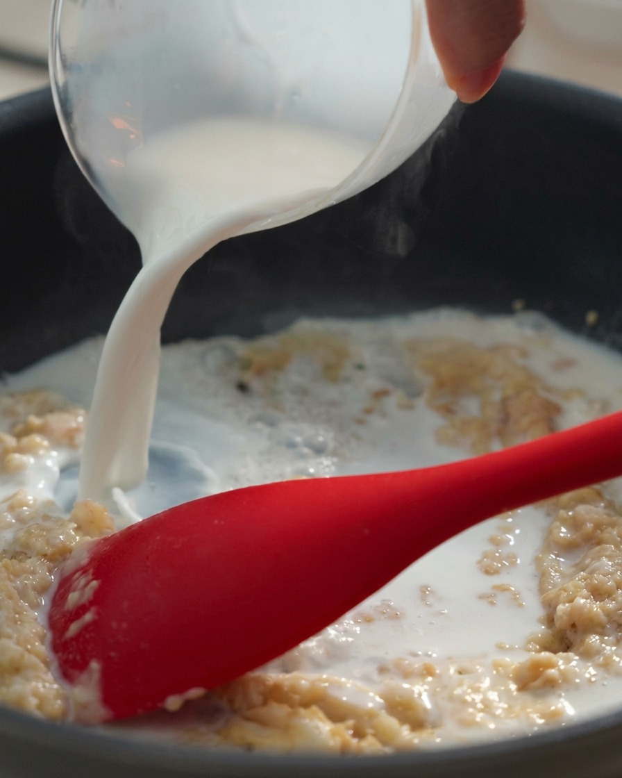 Milch wird aus einem Messbecher in eine Pfanne mit der Butter-Mehl-Mischung gegossen.