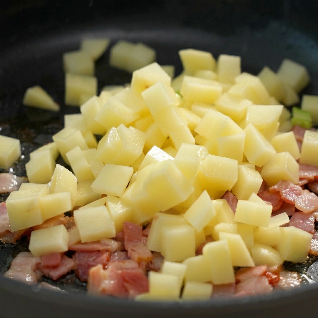 Kartoffelwürfel werden in die Pfanne zum gebratenen Speck gegeben.