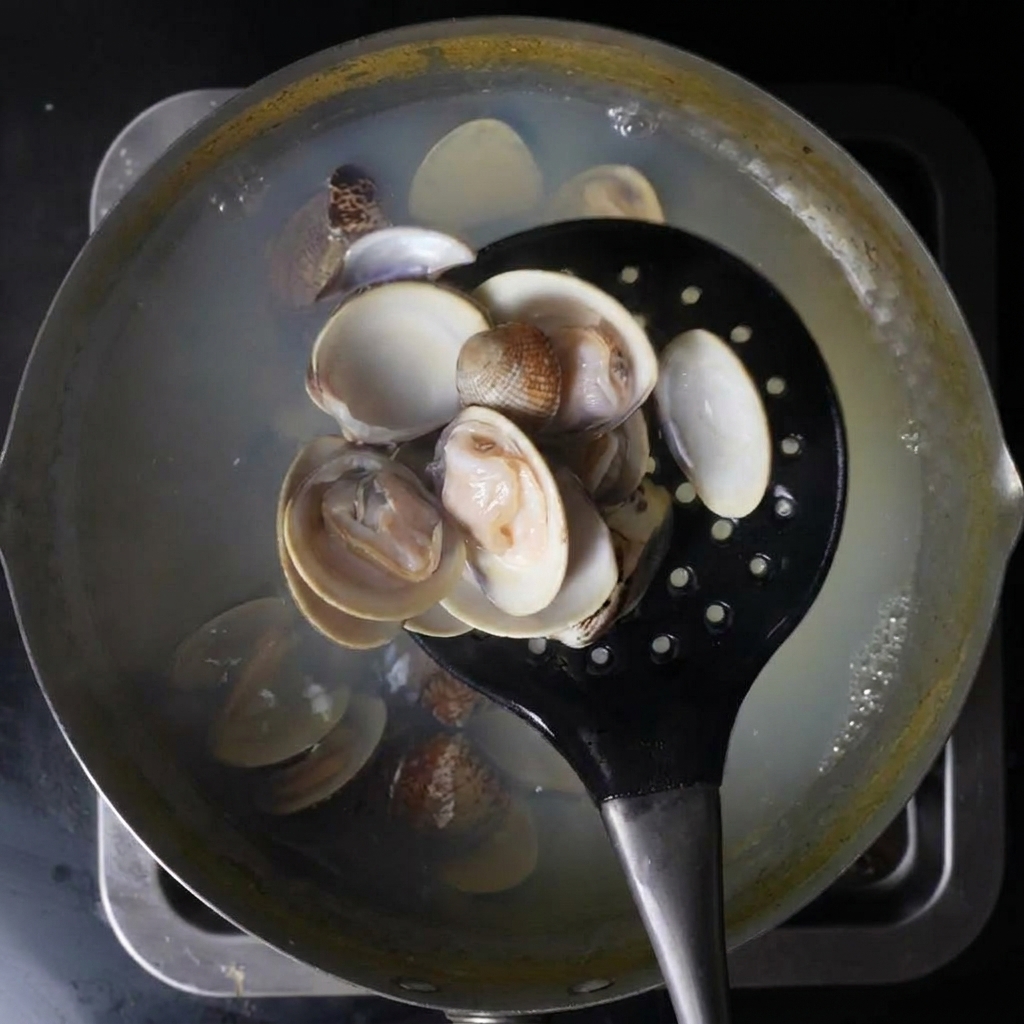 Ein schwarzer Schaumlöffel hebt geöffnete Venusmuscheln aus einem Topf mit kochendem Wasser.