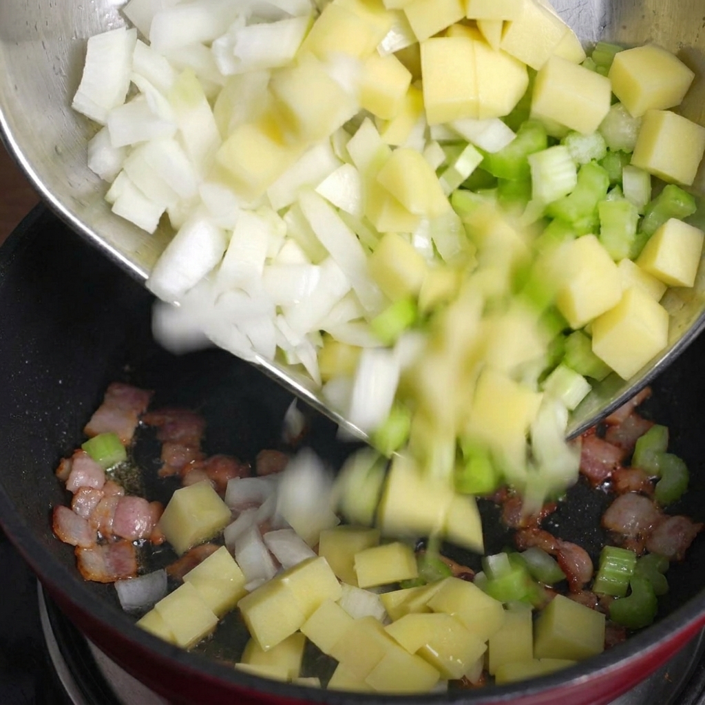 Gewürfelte Kartoffeln, Sellerie und Zwiebeln werden aus einer Metallschüssel in eine Pfanne mit gebratenen Speckstücken geschüttet.