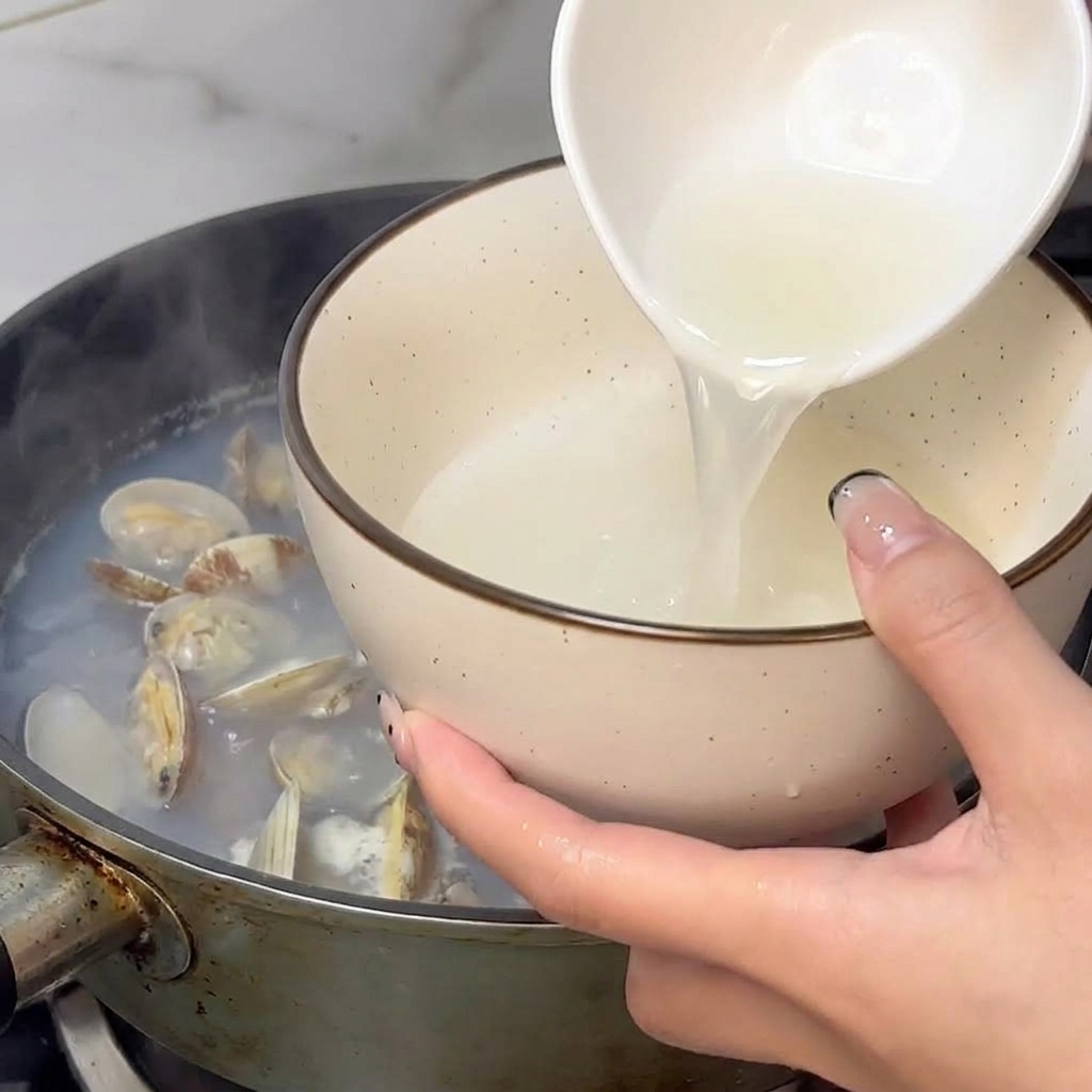 Eine Hand schöpft mit einer kleinen weißen Schale dampfenden Muschelsud aus einem Topf.