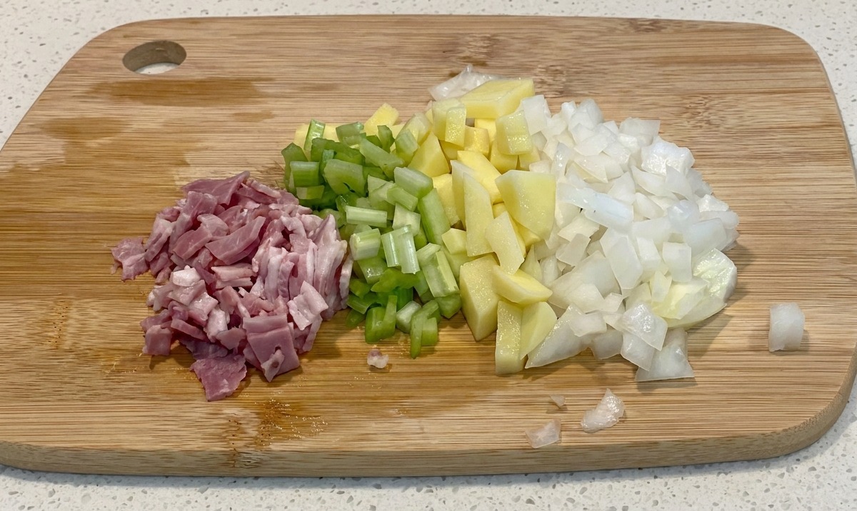 Gewürfelter Speck, Sellerie, Kartoffeln und Zwiebeln liegen ordentlich auf einem Holzschneidebrett.