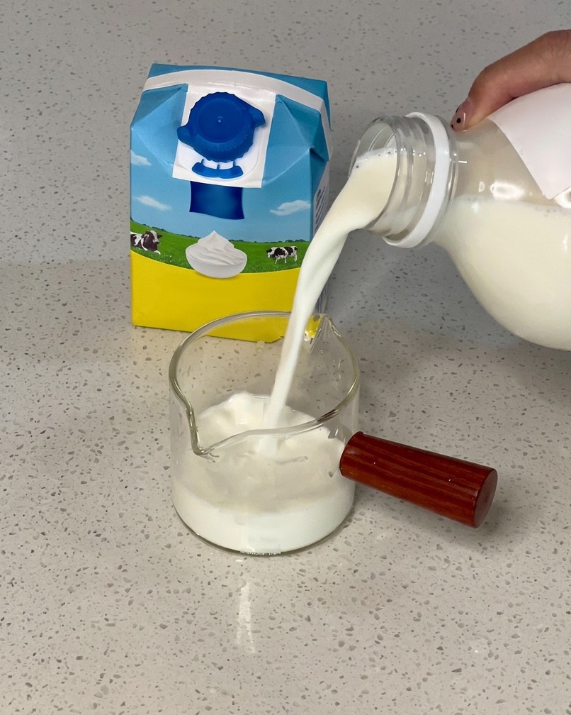 Milch wird aus einem Karton in einen kleinen Glaskrug gegossen, der bereits Sahne enthält.