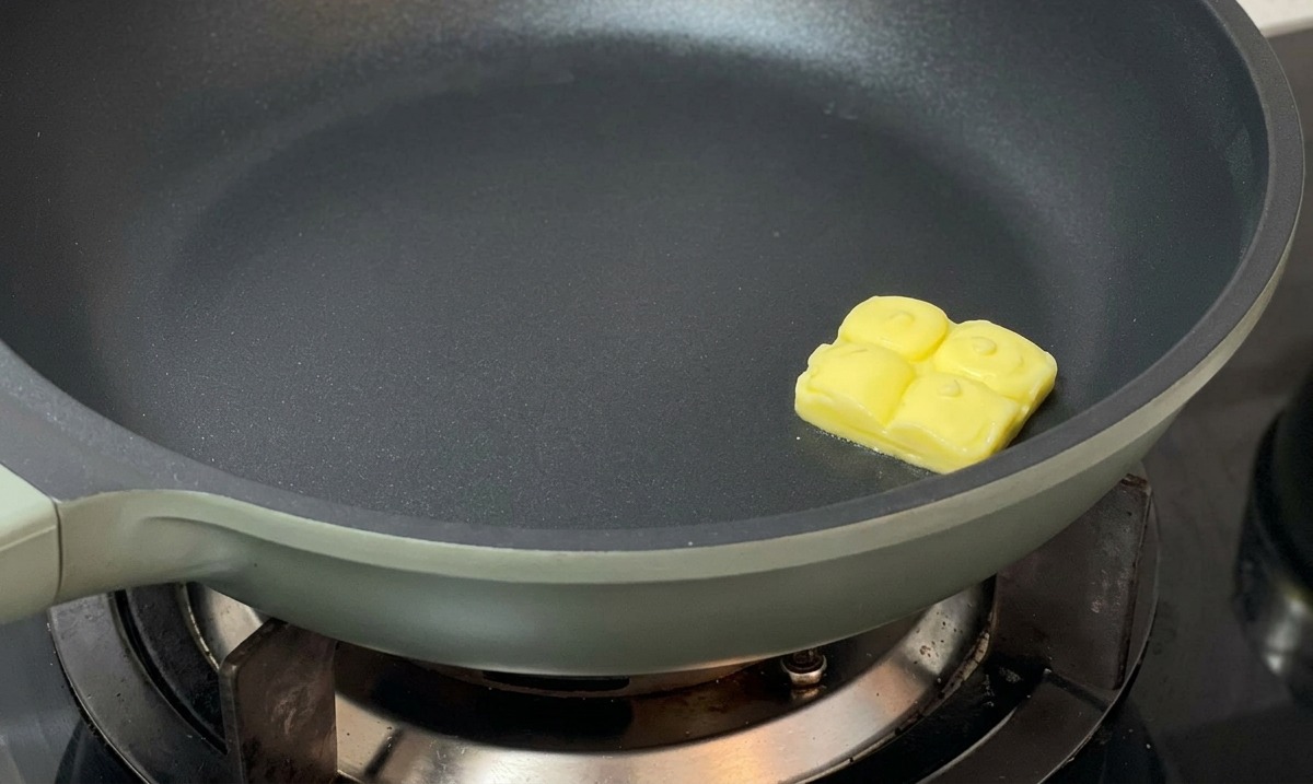 Ein Stück Butter schmilzt in der Mitte einer dunklen, beschichteten Pfanne.
