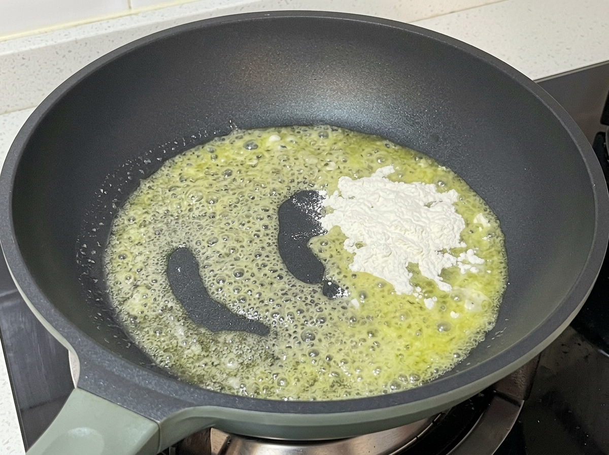 In einer Pfanne wird weißes Mehl in schäumende, geschmolzene Butter eingerührt.