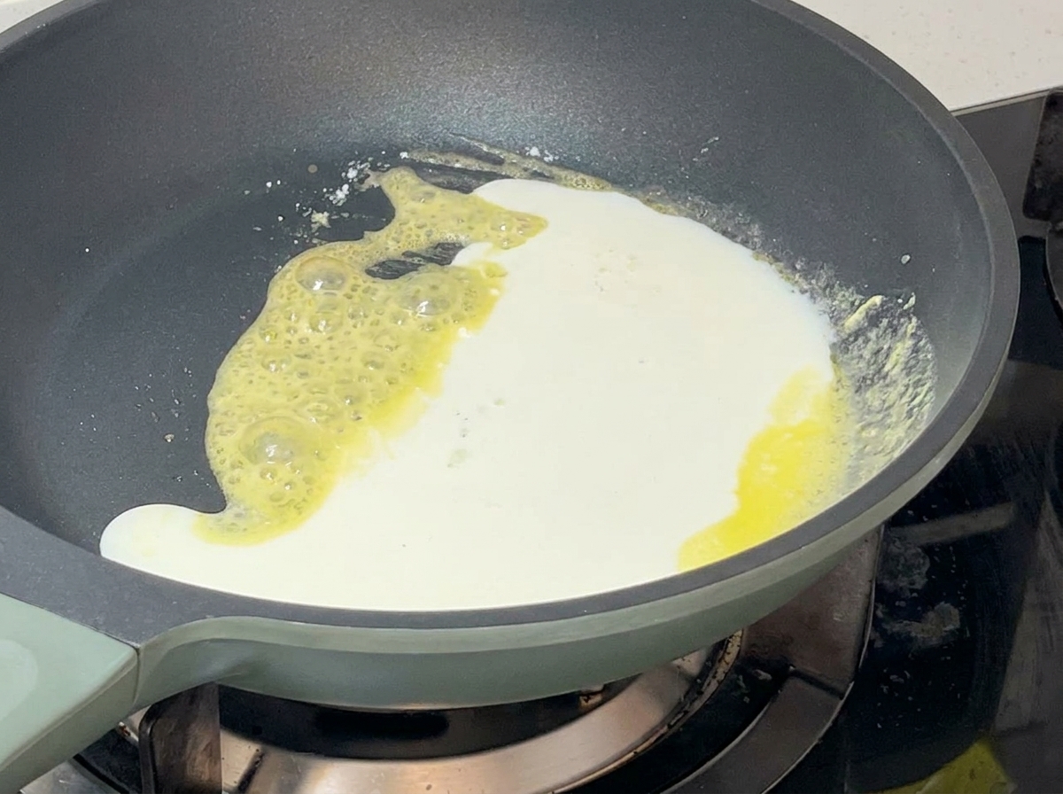 Weiße Milch-Sahne-Mischung wird in die Pfanne zur sprudelnden Mehlschwitze gegossen.