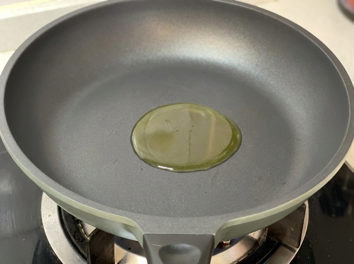 Goldenes Olivenöl in einer sauberen, dunkelgrauen Pfanne auf einem Gasherd.