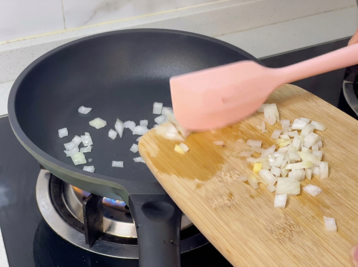 Gewürfelte Zwiebeln werden mit einem Teigschaber vom Schneidebrett in eine heiße Pfanne geschoben.