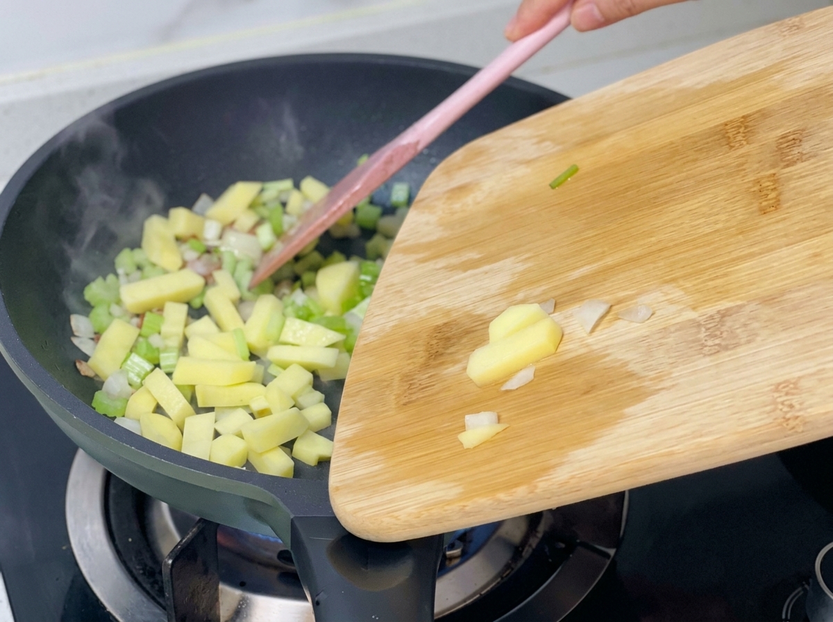 Kartoffelwürfel werden zu den bereits angebratenen Zwiebeln, dem Sellerie und Speck in die Pfanne gegeben.
