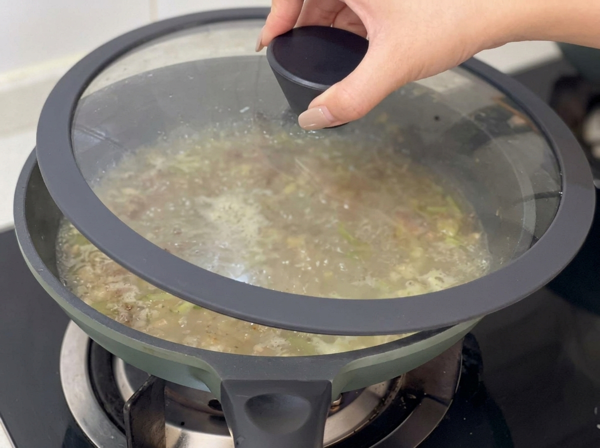 Ein Glasdeckel wird auf die Pfanne mit der köchelnden Muschelsuppe gesetzt.