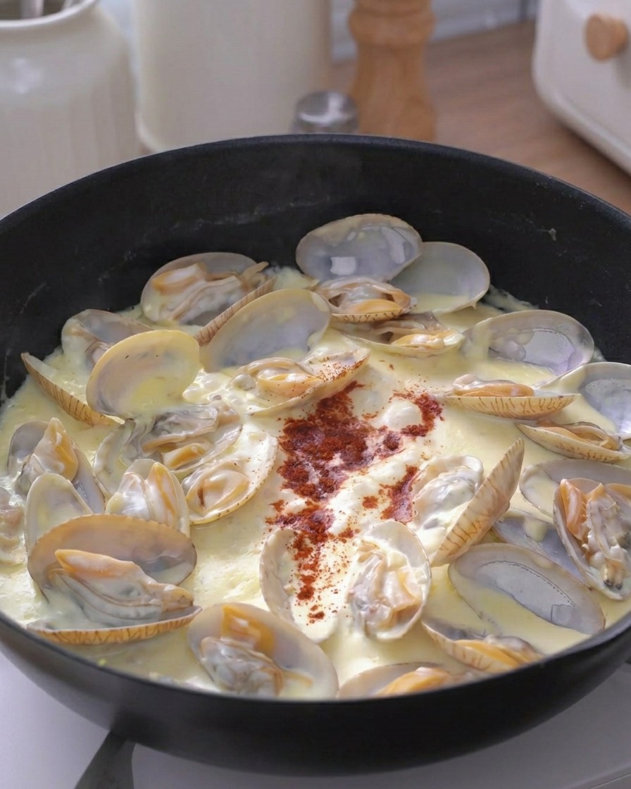 Eine Prise rotes Gewürzpulver wird in die Mitte der cremigen Muschelpfanne gestreut.