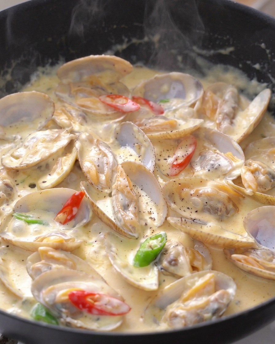 Gegarte Muscheln in Sahnesauce, garniert mit Chili-Scheiben und frisch gemahlenem Pfeffer.