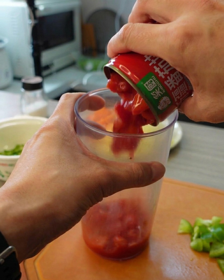 Hände gießen gehackte Dosentomaten aus einer Dose in einen hohen Mixbecher.