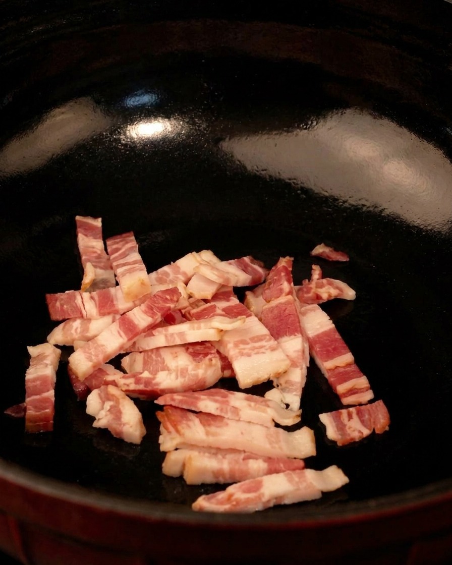 Rohe Speckwürfel in einer schwarzen Pfanne, bereit zum Braten bei mittlerer Hitze.