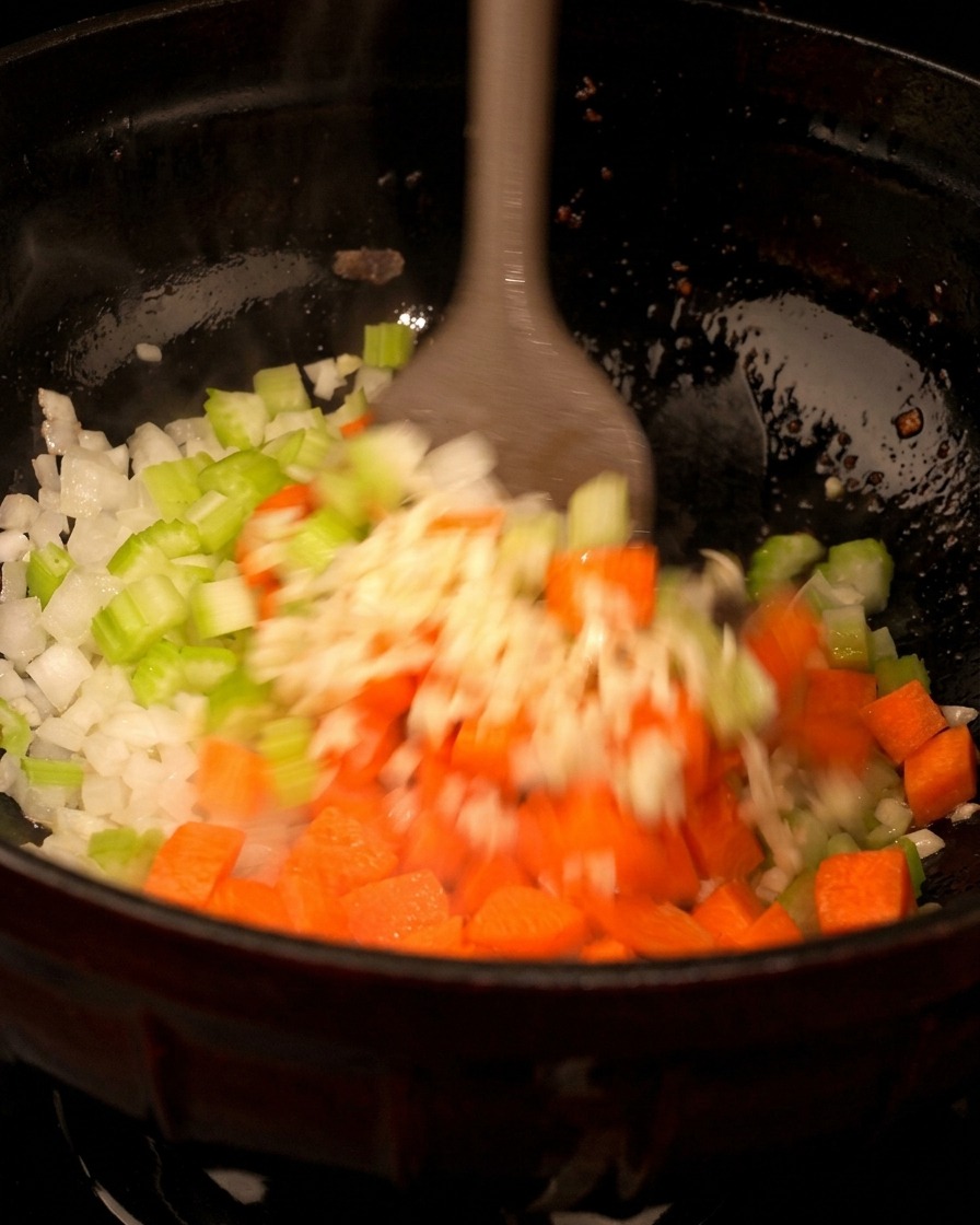 Karottenwürfel werden in eine Pfanne zu gedünsteten Zwiebeln und Sellerie gegeben.