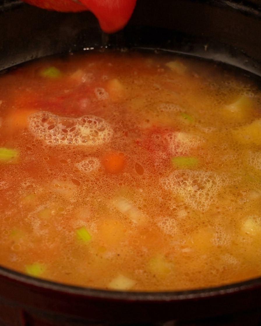 Rotes Tomatenpüree wird in einen Topf mit Brühe und Gemüsestücken gegossen.