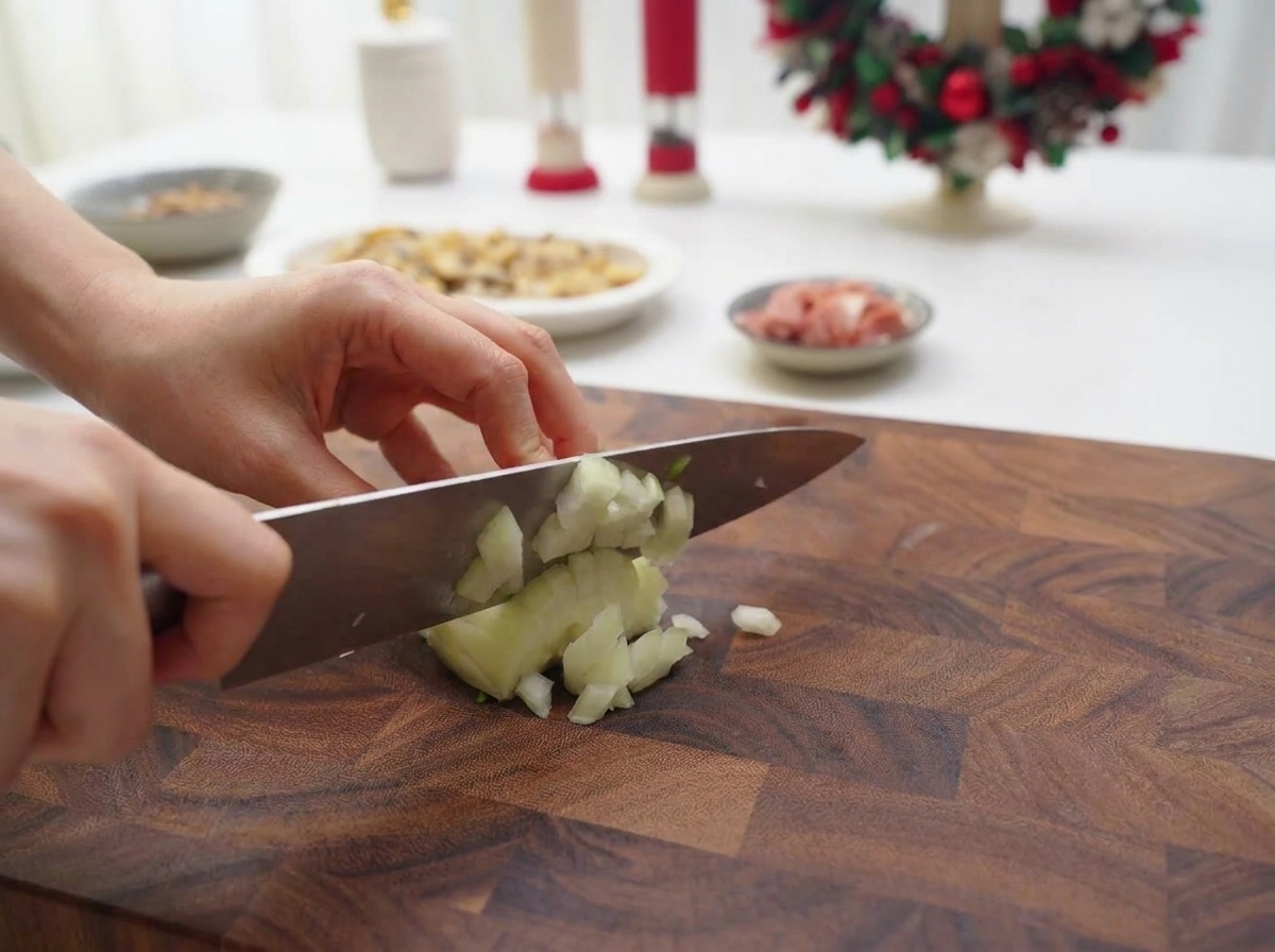 Hände würfeln eine weiße Zwiebel mit einem Kochmesser fein auf einem Holzbrett.