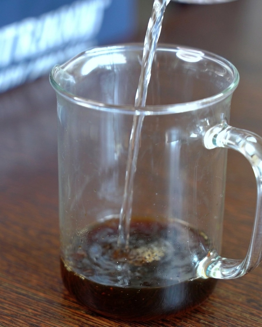 Klares Wasser wird in einen Messbecher gegossen, der eine dunkle Mischung aus Kombu-Sojasauce und Zucker enthält.