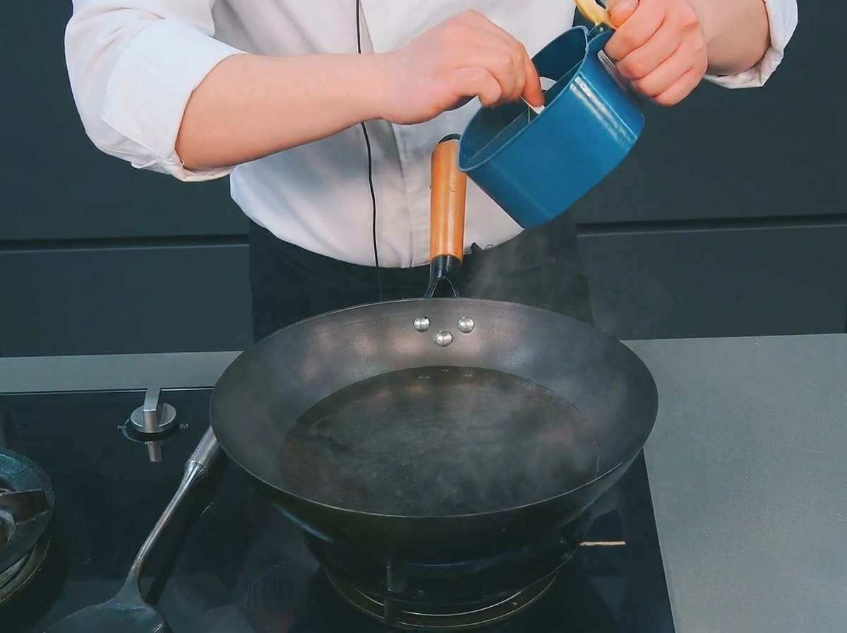 Ein Koch gibt aus einem blauen Behälter einen kleinen Löffel Salz in einen Wok mit dampfendem, kochendem Wasser.