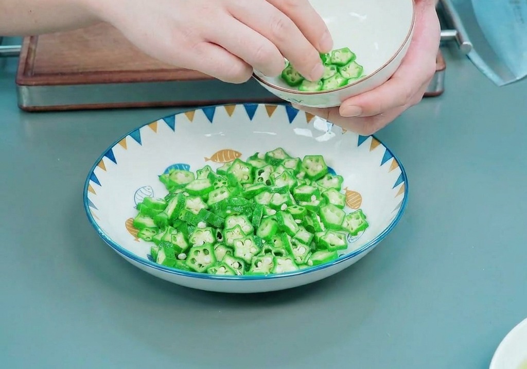 Hände legen die Innenseite einer kleinen weißen Schüssel sorgfältig mit leuchtend grünen, sternförmigen Okrascheiben aus.