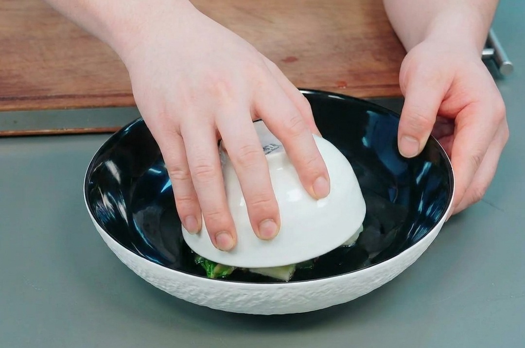 Hände heben vorsichtig eine kleine weiße Schüssel von einer großen schwarzen Schüssel ab, um die geformte Okra-Kartoffel-Kuppel darin zu enthüllen.