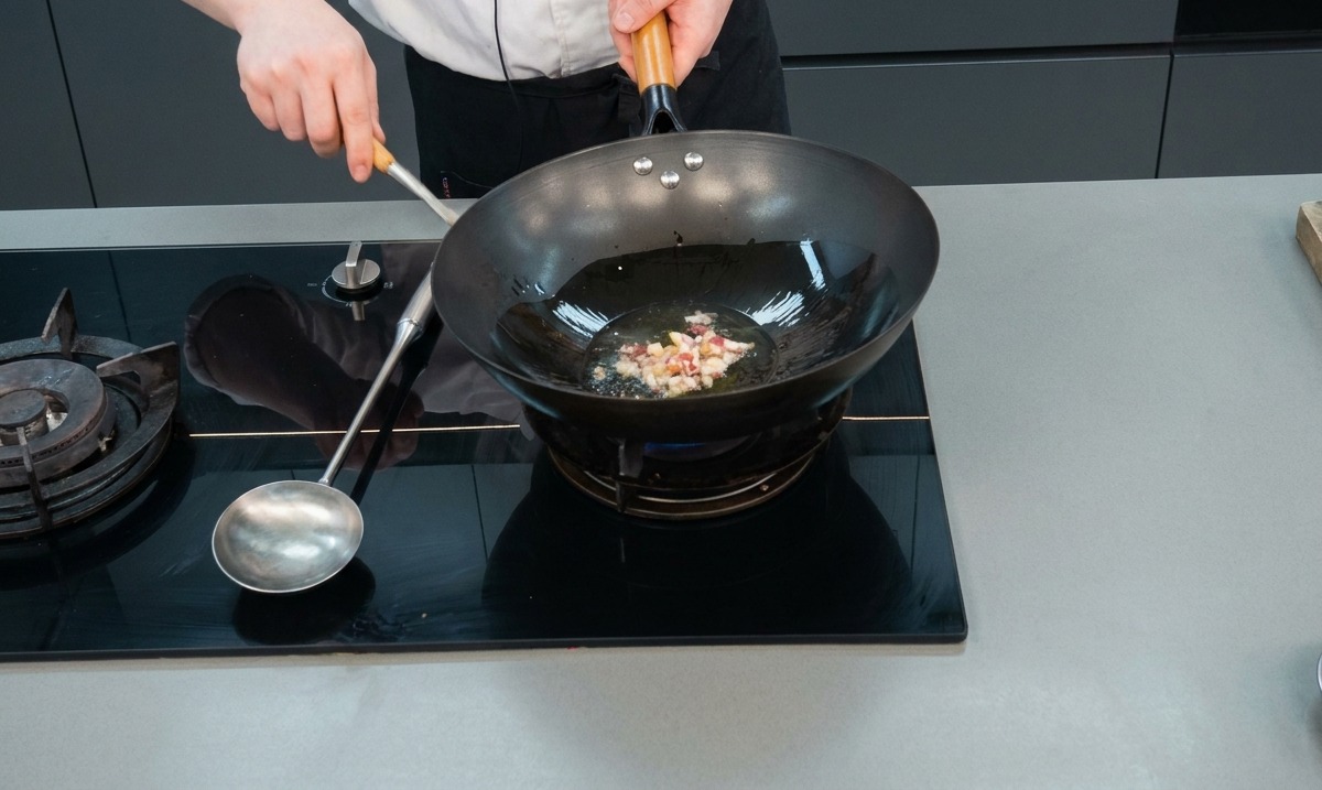 Gewürfeltes gepökeltes Fleisch und Knoblauch brutzeln in heißem Öl in einem schwarzen Wok auf einem Gasherd.