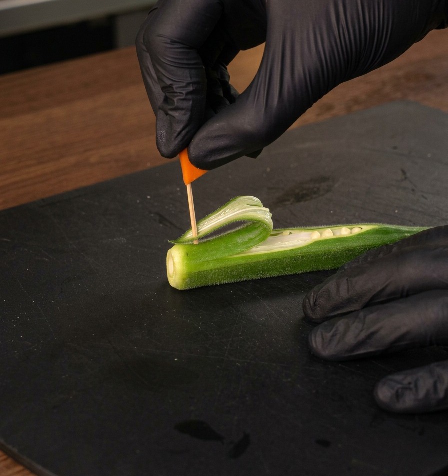Eine Hand steckt eine kleine orangefarbene Karottenflagge auf einem Zahnstocher in das Okra-Segel.