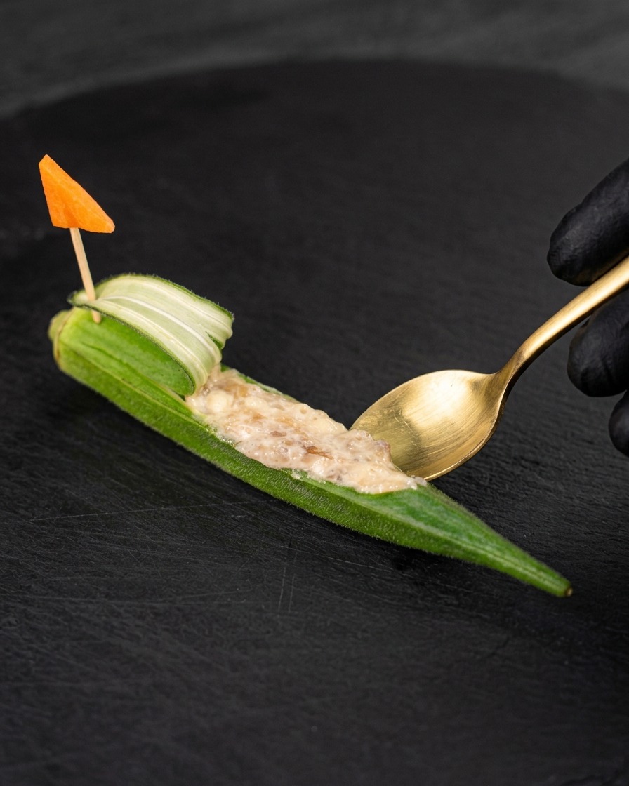 Ein kleiner Löffel füllt die ausgehöhlte Okra mit der rohen Garnelenpaste.
