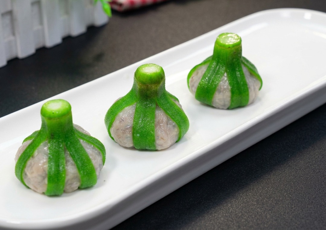 Drei perfekt geformte, mit Okra umhüllte Garnelenbällchen, die verkehrt herum auf einem langen weißen rechteckigen Teller für den Dämpfer bereitstehen.