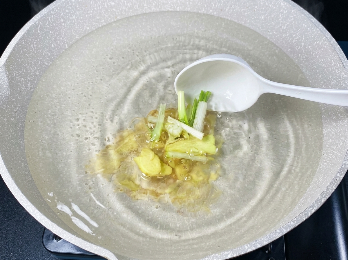 Ingwer und Frühlingszwiebeln werden mit einer Kelle in kochendes Wasser gegeben.