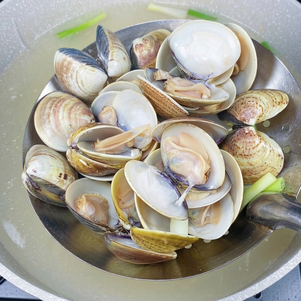 Eine Schaumkelle hält frisch gekochte, geöffnete Muscheln über dem Topf.