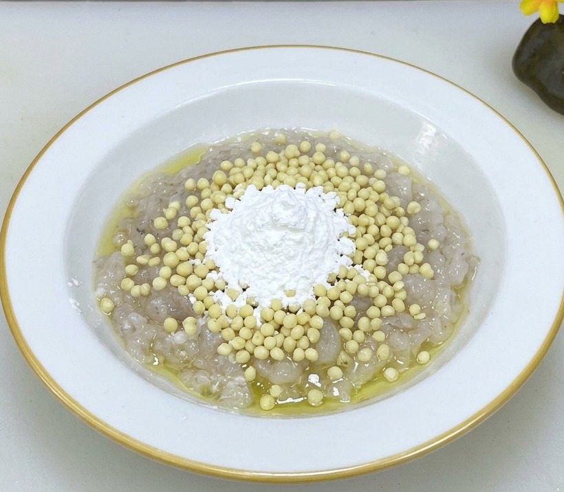 Eine weiße Schüssel mit roher Garnelenpaste, bestreut mit Okrakernen und Maisstärke.