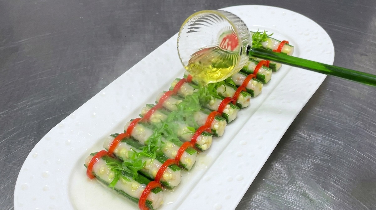 Heißes Öl wird aus einer Schöpfkelle über die gedämpfte Okra mit Zwiebeln und Chili gegossen.