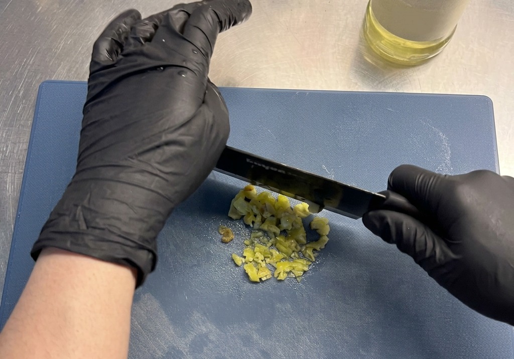 Gelbe eingelegte Chilis werden auf einem blauen Schneidebrett fein gehackt.