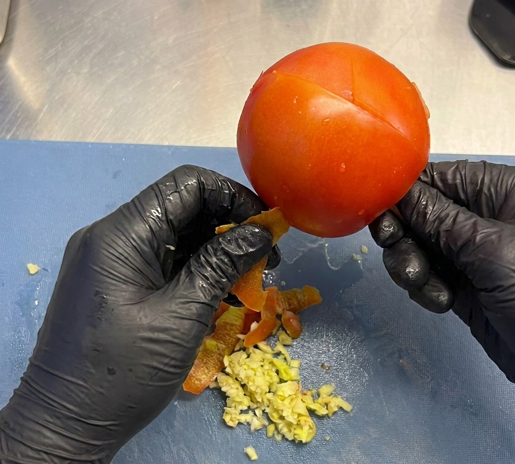 Vorsichtiges Abziehen der Haut von einer reifen roten Tomate.
