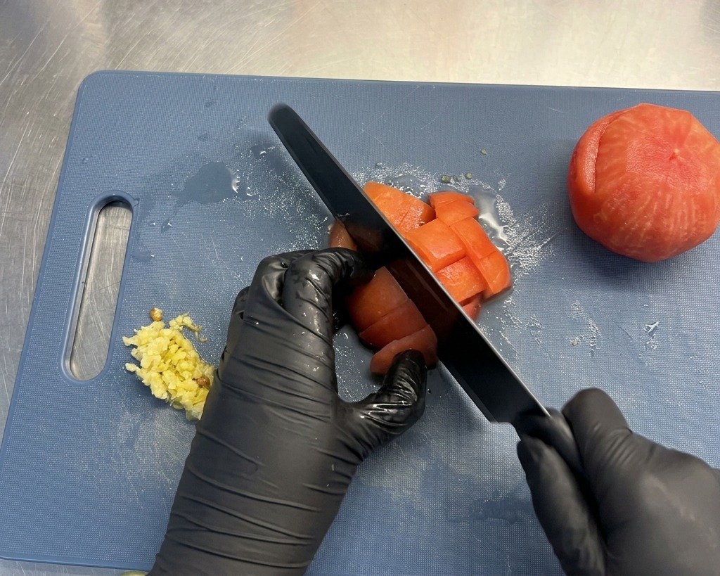 Eine geschälte Tomate wird auf einem Schneidebrett in kleine Würfel geschnitten.