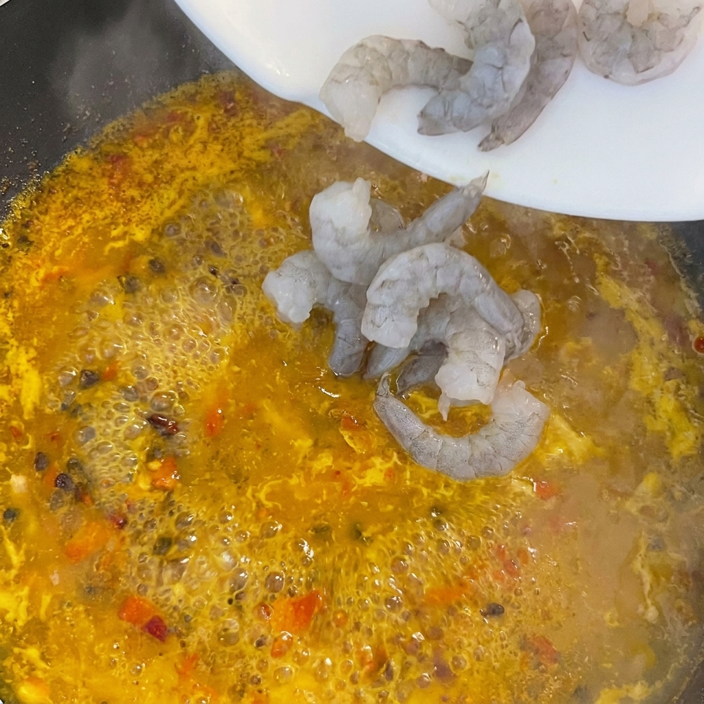 Rohe Garnelen werden in die kochende gelbe Brühe gegeben.