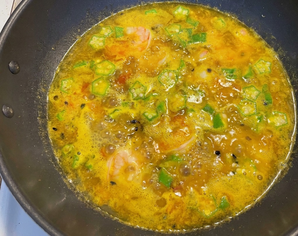 Fertige Suppe im Wok mit rosa Garnelen, grüner Okra und Passionsfruchtkernen.