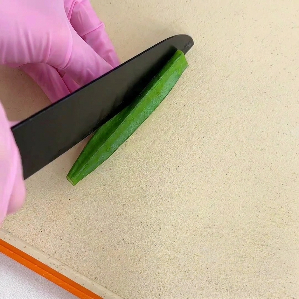 Halbieren einer blanchierten Okraschote der Länge nach mit einem schwarzen Messer.