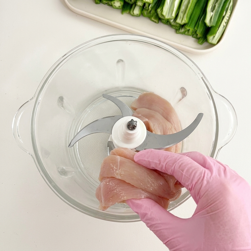 Hähnchenstücke werden in einen Glasbehälter eines Mixers mit Metallklingen gegeben.