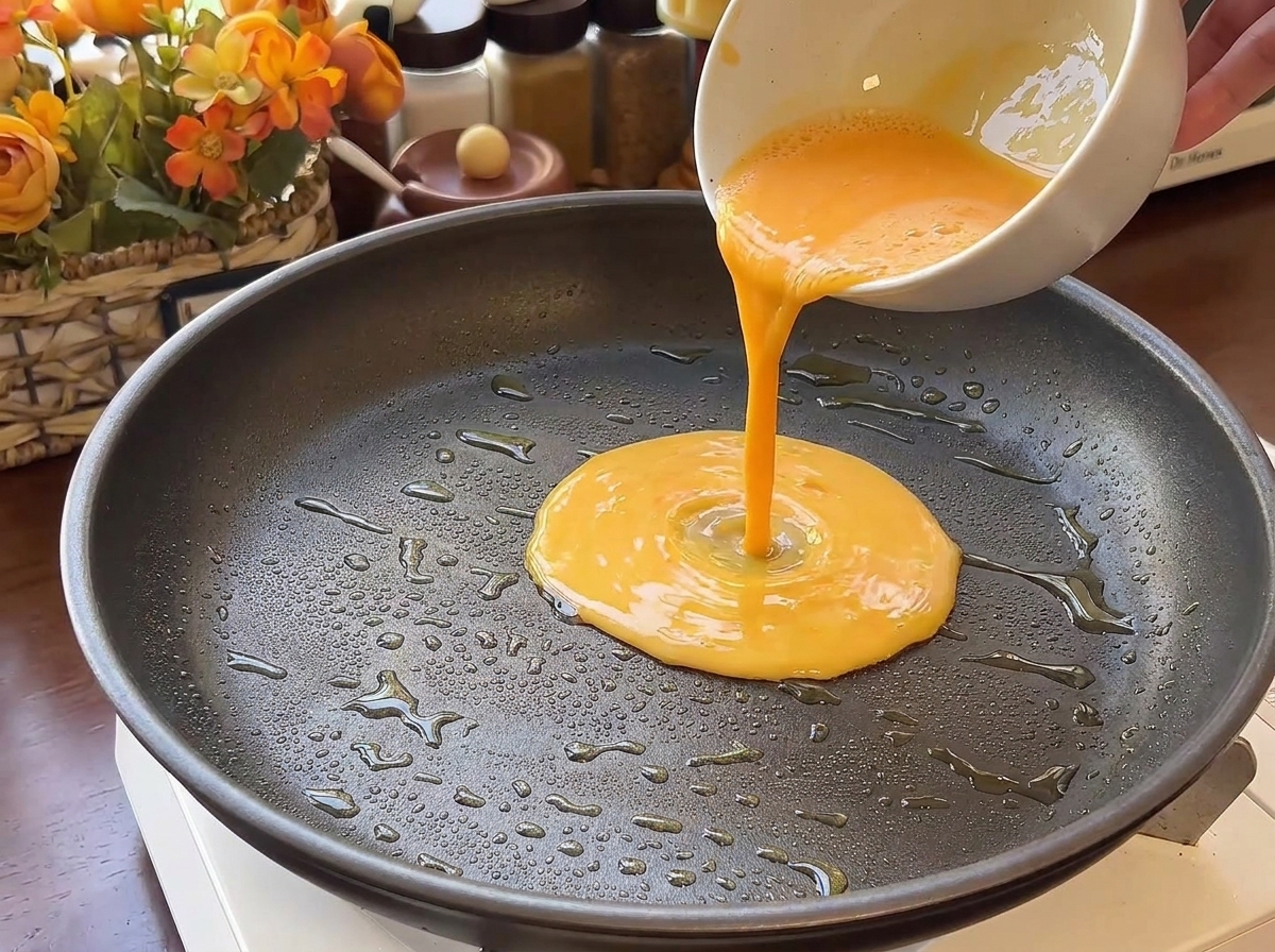 Flüssiges Ei wird in eine heiße, beschichtete Bratpfanne mit etwas Öl gegossen.