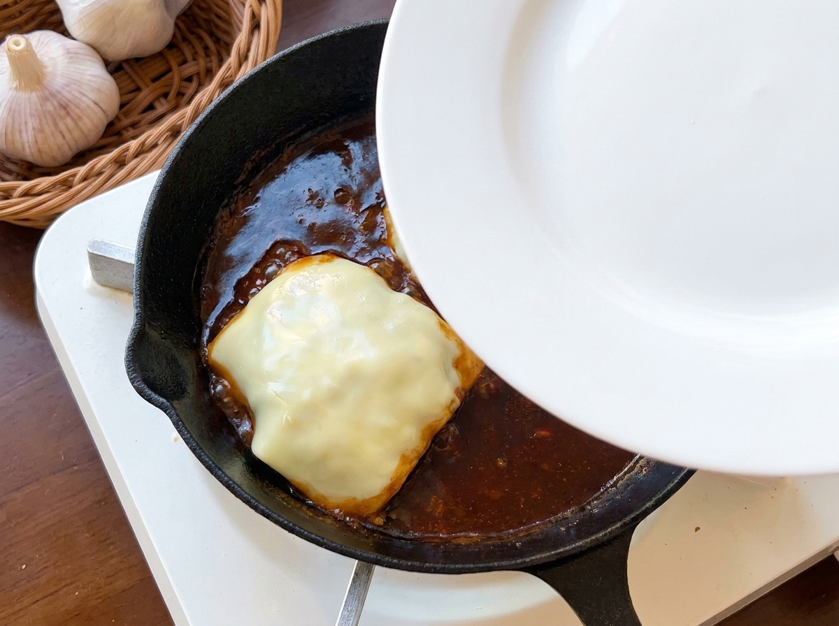 Ein Teller wird als Deckel auf eine Pfanne mit dem Käse-Patty gelegt.