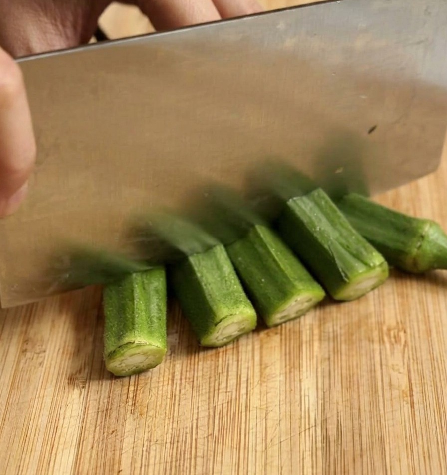 Frische grüne Okra wird mit einem großen Messer in dicke Scheiben geschnitten.
