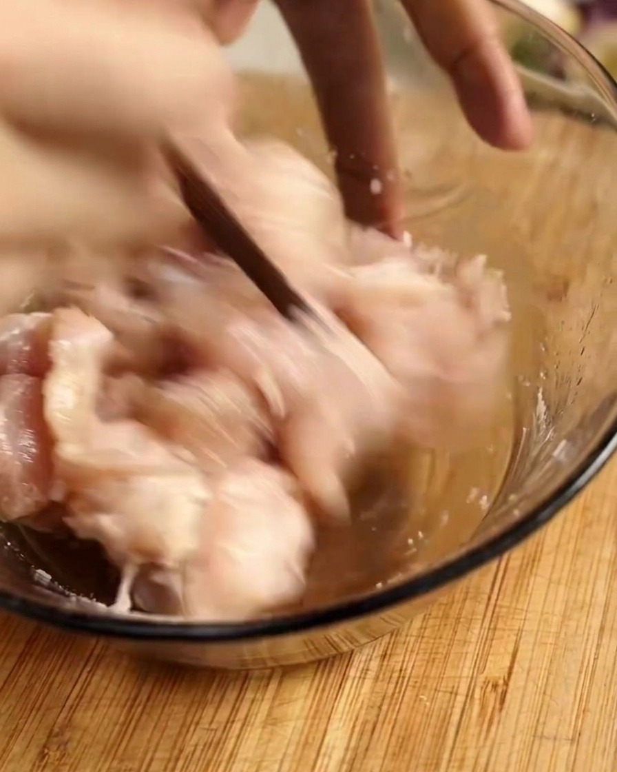 Rohe Hähnchenstücke werden mit Stäbchen in einer Glasschüssel mit Marinade vermengt.