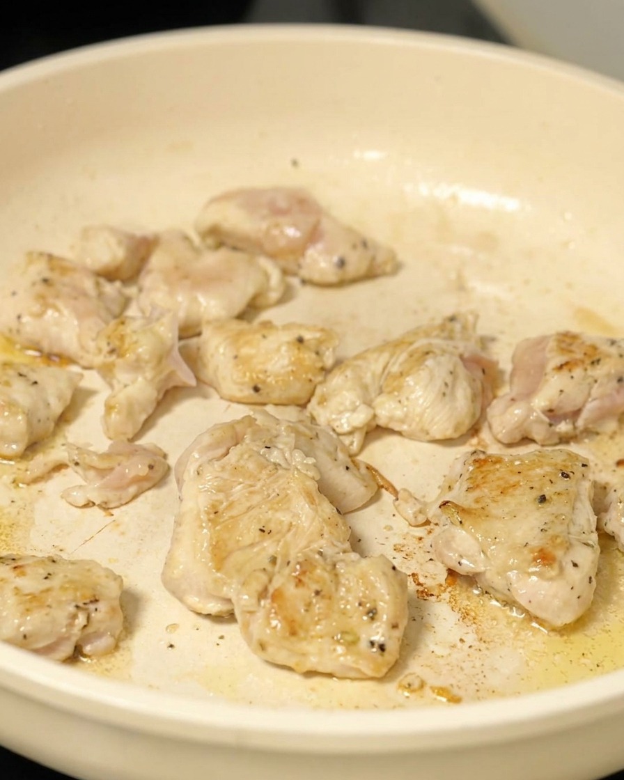 Hähnchenwürfel werden in einer Pfanne angebraten, bis sie leicht gebräunt sind.