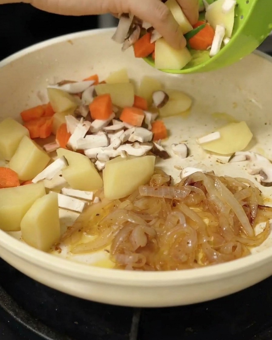 Kartoffelstücke, Karotten und Shiitake-Pilze werden zu den Zwiebeln in die Pfanne gegeben.